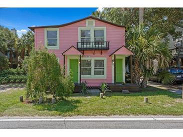 Charming pink two-story home with a small balcony, green doors, and lush landscaping at 509 E Ashley Ave, Folly Beach, SC 29439