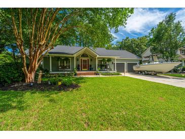 Charming single-story home featuring mature trees, a lush lawn, and a quaint covered front porch with a boat on the driveway at 1098 Blue Marlin Dr, Charleston, SC 29412