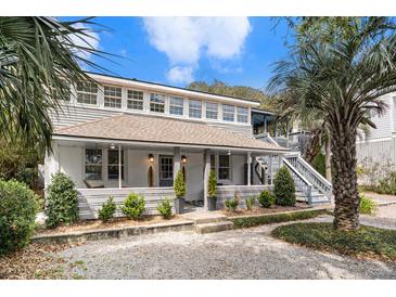 Charming two-story home featuring a welcoming front porch, lush landscaping, and a side staircase to a deck at 504 W Ashley Ave, Folly Beach, SC 29439