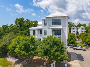 Stylish three-story home featuring a white metal roof and beautifully landscaped surroundings with mature trees at 992 Key Colony Ct, Mount Pleasant, SC 29464