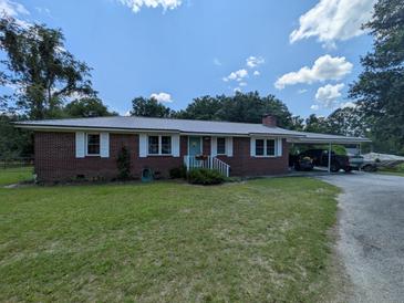 Charming red brick single-story home featuring a metal roof, carport, and well-maintained landscaping at 205 Indian Field Cir, Saint George, SC 29477