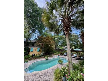 A backyard pool is surrounded by a brick patio, tropical foliage, and mature trees at 2066 Wappoo Dr, Charleston, SC 29412