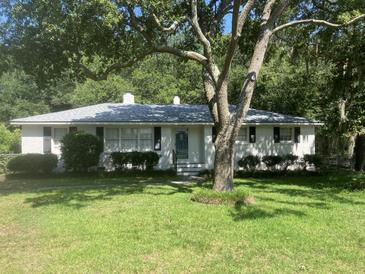 Charming, single-story home with a white brick exterior, a gray roof, and surrounded by lush greenery at 874 Evans Rd, Charleston, SC 29412