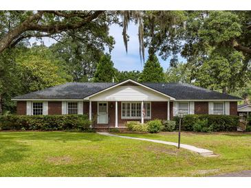 Charming brick home featuring a well-manicured lawn, crisp white shutters and surrounded by mature trees at 1789 Balfoure Dr, Charleston, SC 29407