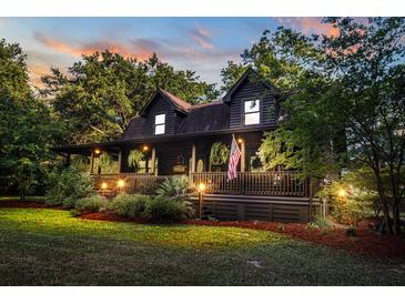 Charming log home with covered porch, manicured lawn, and warm exterior lighting at 24678 Augusta Hwy, Cottageville, SC 29435