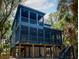 Exterior of elevated stilt house with screened-in porch and blue paneling amongst green trees and vegetation at 615 Pompano St, Edisto Island, SC 29438