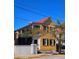 Charming yellow two-story home with a red roof, black shutters, white picket fence, and lush landscaping at 167 Coming St, Charleston, SC 29403