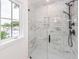 Elegant glass enclosed shower with white marble tile surround and black fixtures, brightened by a window at 24 Iron Frg Aly, Charleston, SC 29403