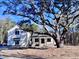 Charming two-story home featuring white siding, brick foundation, and a welcoming front porch, all shaded by a mature tree at 3874 Srevir Rd, Johns Island, SC 29455