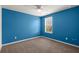 A simple bedroom with blue walls, carpeted floors, and a window offering natural light at 9747 Roseberry Street, Ladson, SC 29456