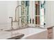 Close-up of a farmhouse sink with elegant fixtures, complemented by marble countertops and a bright, window-filled backdrop at 15 Watroo Pt, Daniel Island, SC 29492