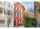 A narrow red brick home with blue shutters is flanked by white brick house and mature trees at 32 Tradd St, Charleston, SC 29401