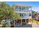 Exterior shot of a three-story blue house with double porches, lush trees, and ample parking at 74 Sandbar Ln, Folly Beach, SC 29439