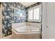 Cozy bathroom featuring a corner bathtub, wallpaper, and a window with plantation shutters for natural light at 1756 Indigo Island Dr, Hanahan, SC 29410