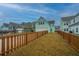 Large backyard with a wooden fence, featuring freshly installed lawn, neighboring homes, and blue skies at 219 Corvus St, Summerville, SC 29483