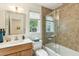 Bright bathroom features a vanity, toilet, and tiled shower-tub combo with glass doors at 608 W Beach Ct, Folly Beach, SC 29439