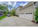 View of a multi-car garage with white doors, a wide driveway, and mature landscaping at 6934 Tanner Hall Blvd, Hanahan, SC 29410