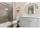 Bright bathroom featuring a white double vanity, round mirror, and glass-enclosed shower with neutral tile at 112 E Huron Ave # C, Folly Beach, SC 29439