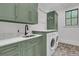 Well-lit laundry room with sage green cabinets, gold hardware, herringbone floors and white washer/dryer at 215 Fell Pt, Daniel Island, SC 29492