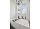 Bright bathroom featuring a modern white tub, black faucet, white marble-look walls, and natural light from windows at 2621 Anchor Watch Dr, Wadmalaw Island, SC 29487