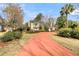 View of the yellow home framed with palms and trees, showcasing a curved red driveway at 941 Law Ln, Mount Pleasant, SC 29464