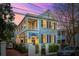 Charming two-story home with double porches, shutters, and lush landscaping at twilight at 100 Queen St, Charleston, SC 29401