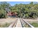 A wooden pier leads to a charming home with red roof and white siding surrounded by lush trees at 127 Oak St, McClellanville, SC 29458