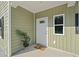 Charming front porch with olive green vinyl siding, a white door, and decorative plants welcoming guests at 1738 N N Hwy 52, Bonneau, SC 29431