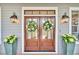 Elegant wooden double doors adorned with wreaths, flanked by potted plants and stylish lighting fixtures at 4162 Ten Shillings Way, Hollywood, SC 29470