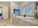 Luxurious bathroom featuring a soaking tub, a wall-mounted TV, and a serene window view at 4385 Ten Shillings Way, Hollywood, SC 29470