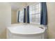 Bright bathroom featuring a corner tub with blue curtains and a mirrored wall that enhances the light from the nearby window at 754 Miriam Ln, Ridgeville, SC 29472