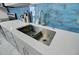 Close up of a stainless steel kitchen sink with grey cabinets, white quartz countertops, and blue subway tile backsplash at 3651 Barton St, Johns Island, SC 29455