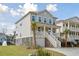 A picturesque two-story beach house with a white staircase, complemented by lush green landscaping and blue sky at 2280 Minfarm Way # 529, Mount Pleasant, SC 29466