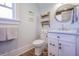 Bright bathroom with a window, white vanity, round mirror, and open shelving displaying decorative towels at 1174 Hitchfield Ln, Awendaw, SC 29429