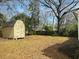 Shed in a backyard with trees, shrubs and leaf covered ground with a partial view of a house at 1610 Larry St, North Charleston, SC 29406