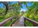 Wooden boardwalk with railings leads to a gated entryway, surrounded by lush greenery and moss-covered trees under a blue sky at 8661 Refuge Point Cir, North Charleston, SC 29420