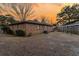 An angled view of a brick house and yard surrounded by a wooden fence with trees against an orange sunset at 7753 Linsley Dr, North Charleston, SC 29418
