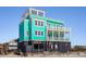 Beautiful beach home with a teal exterior, multiple balconies, and elevated construction on a sandy lot at 1699 E Ashley Ave # B, Folly Beach, SC 29439