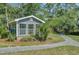 Charming cottage exterior featuring large windows, gray shingles, and surrounding lush greenery and a sidewalk at 8704 Middleton Point Ln, Edisto Island, SC 29438