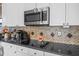 Close-up of the kitchen featuring stainless steel microwave and cooktop over granite countertops with tile backsplash at 9394 Harroway Rd, Summerville, SC 29485