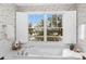 Soaking tub with white shutters and tranquil outdoor views in a stylish bathroom at 3034 Maritime Forest Dr, Johns Island, SC 29455