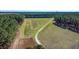 Aerial shot of a long, curving dirt road leading through a grassy field, framed by a dense forest at 732 Lindhaven Dr, Pineville, SC 29468