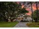 Charming exterior featuring a sprawling lawn, mature trees, and a classic white facade, all complemented by a scenic sunset backdrop at 1456 Mcpherson Lndg, Johns Island, SC 29455