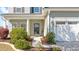 Close-up of the home's entrance with a welcoming porch, lush landscaping, and a two-car garage at 3016 Adventure Way, Ladson, SC 29456