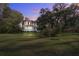 Charming two-story home at dusk with a manicured lawn and mature trees draped with Spanish moss at 8115 Adams Run School Rd, Adams Run, SC 29426