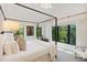 Bedroom with a four-poster bed, white linens, and large windows framing views of lush greenery at 204 E Huron Ave, Folly Beach, SC 29439