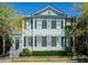 Charming two-story home featuring light blue siding, black shutters, and a welcoming front porch, enhanced by lush landscaping at 740 Stucco Ln, Mount Pleasant, SC 29464