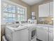 Functional laundry area with washer, dryer, storage cabinets, and a sunlit window at 5758 Chisolm Rd, Johns Island, SC 29455