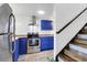 Charming kitchen boasts blue cabinets, stainless steel appliances, and uniquely tiled countertops adjacent to the wooden staircase at 1617 Balsam St, Charleston, SC 29407