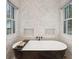 Close-up of luxurious soaking tub with marble-look walls and natural light from large windows at 6 Beverly Rd, Charleston, SC 29407